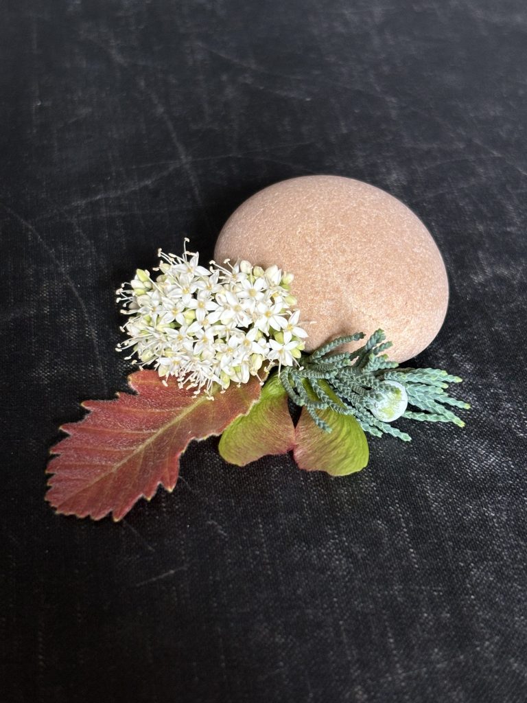 Close up of stone, flowers, and leaves on a black cloth background.